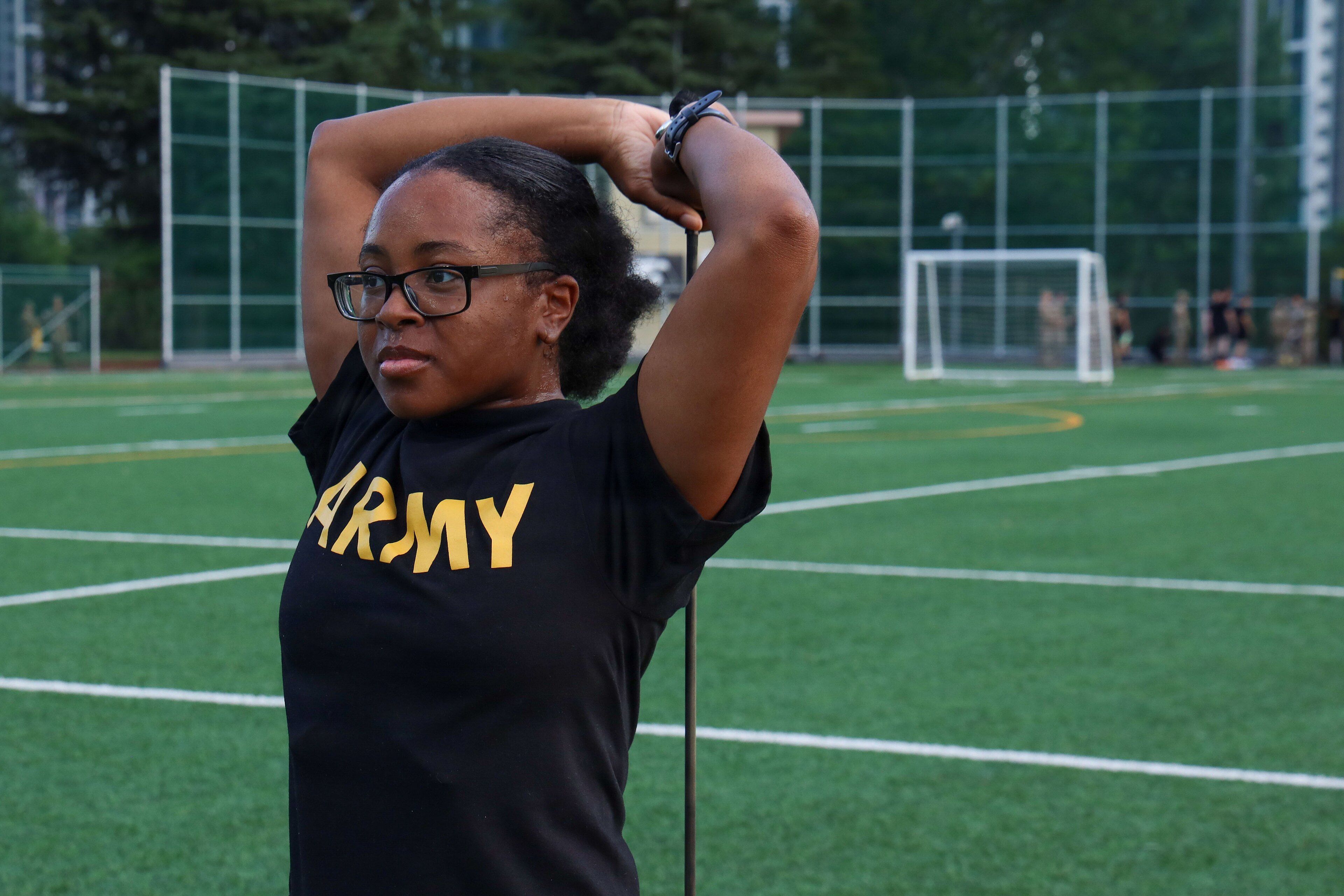 Une pratiquante tire une bande de résistance derrière sa tête, coudes levés, sur un terrain de sport